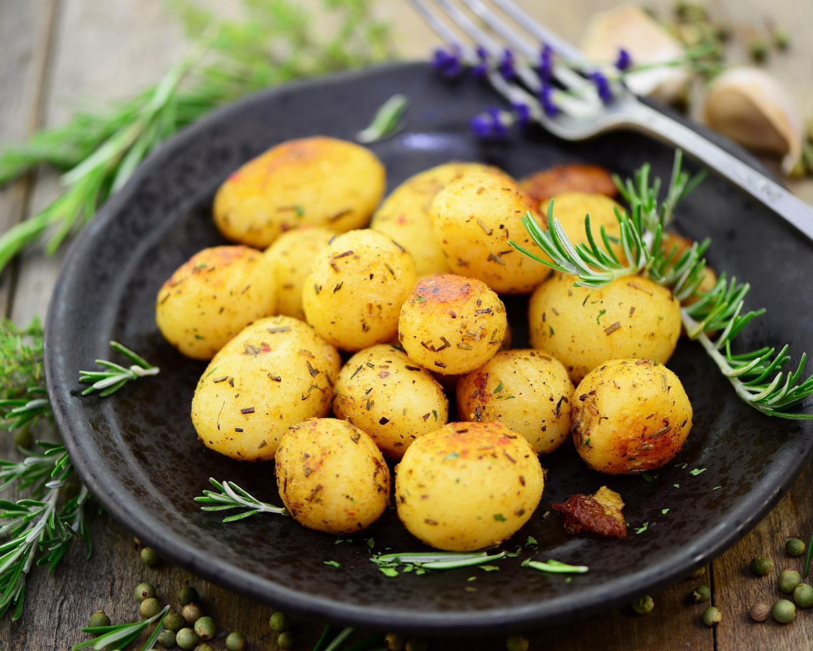 Goldbraun gebratene kleine Kartoffeln mit Rosmarin auf einem dunklen Teller